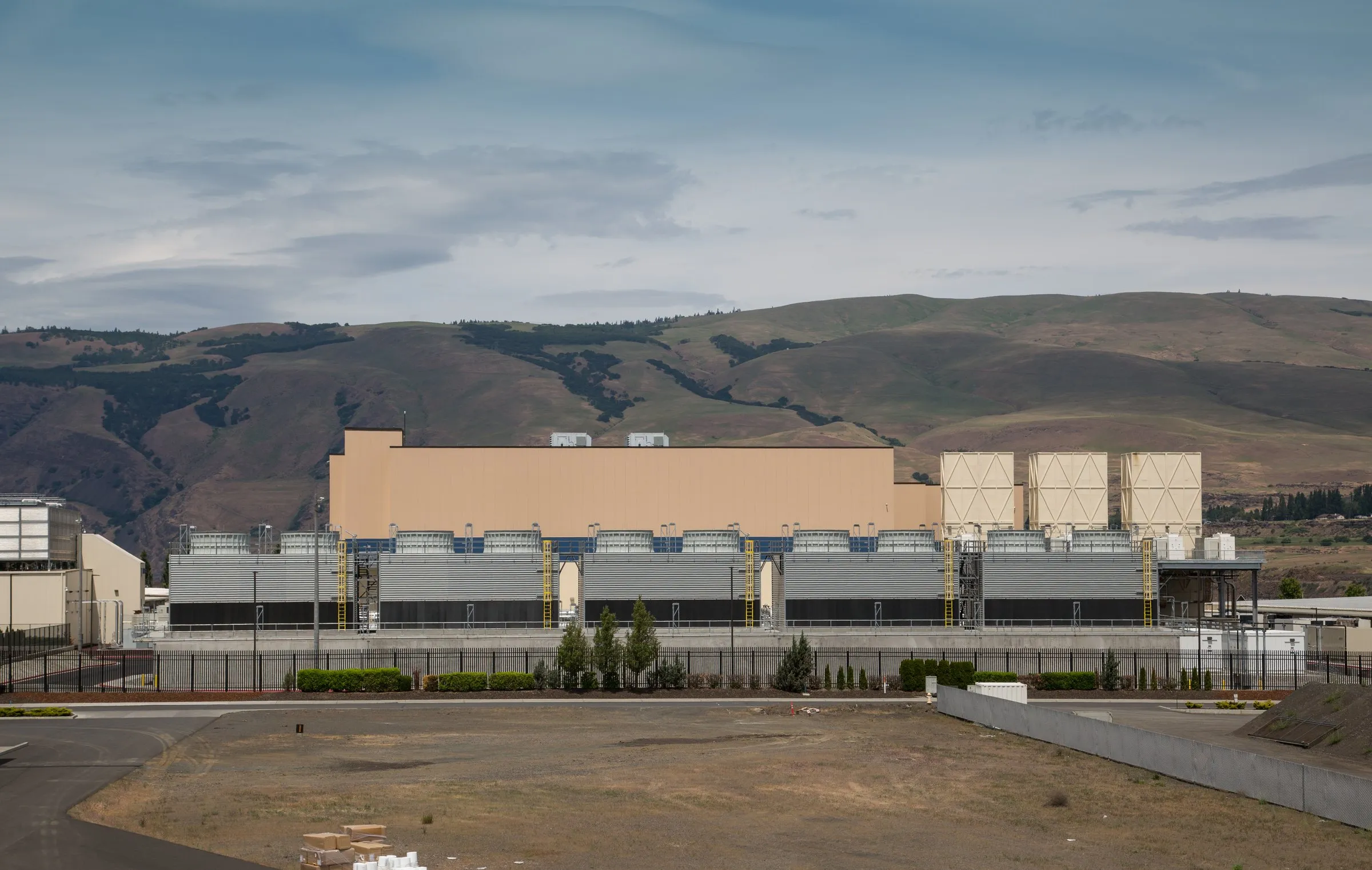 A Google data center in The Dalles, Oregon, its long windowless hall and rows of cooling towers set against dry hills.